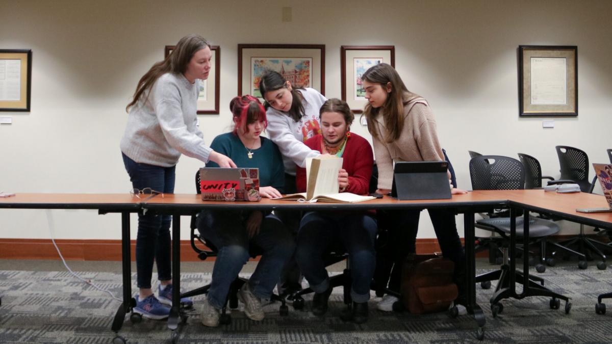 Students and a professor hover over a book.